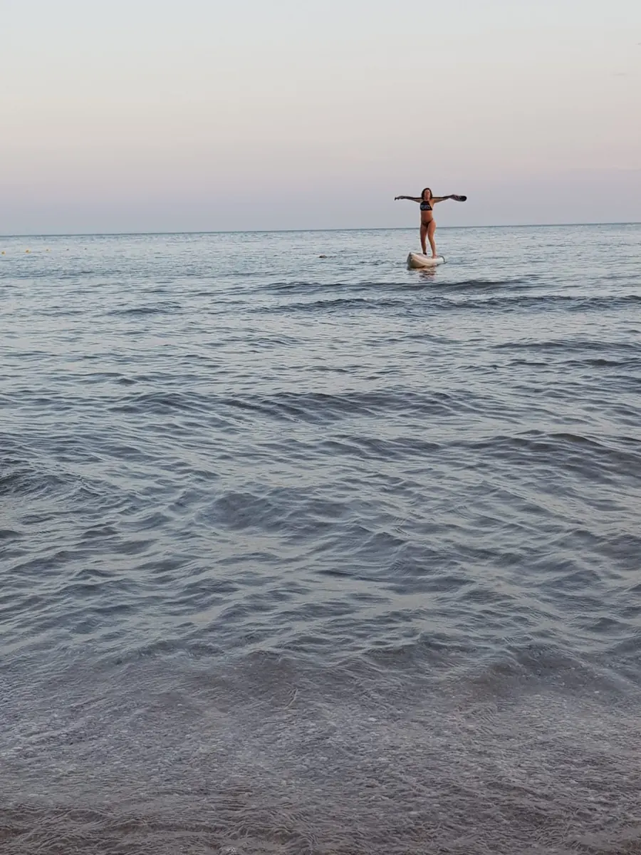 Eli standing on her paddle board at dusk, arms wide open
